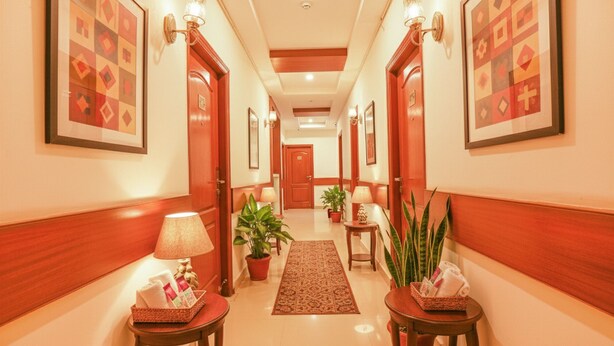 Un pasillo de hotel con paneles de madera, obras de arte enmarcadas, plantas en macetas y una alfombra central.