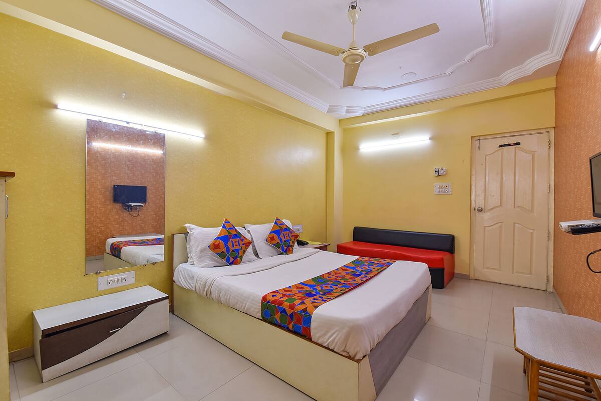 Una habitación de hotel con cama, mesita de noche, banco y ventilador de techo.