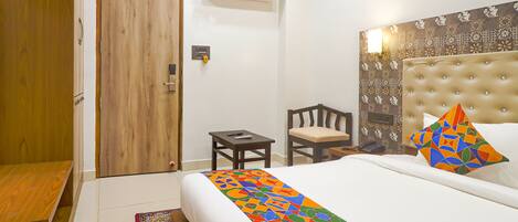 A hotel room with a bed, a small table, a chair, a wardrobe, and an air conditioning unit.