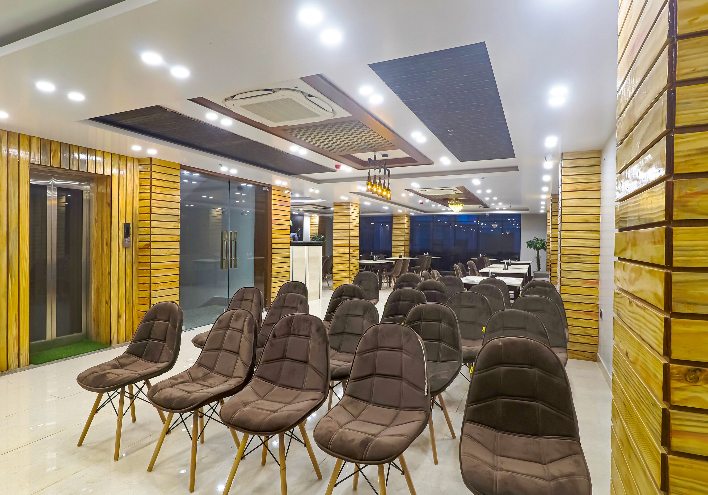 A conference room with rows of brown upholstered chairs, a reception desk, and a modern ceiling design.