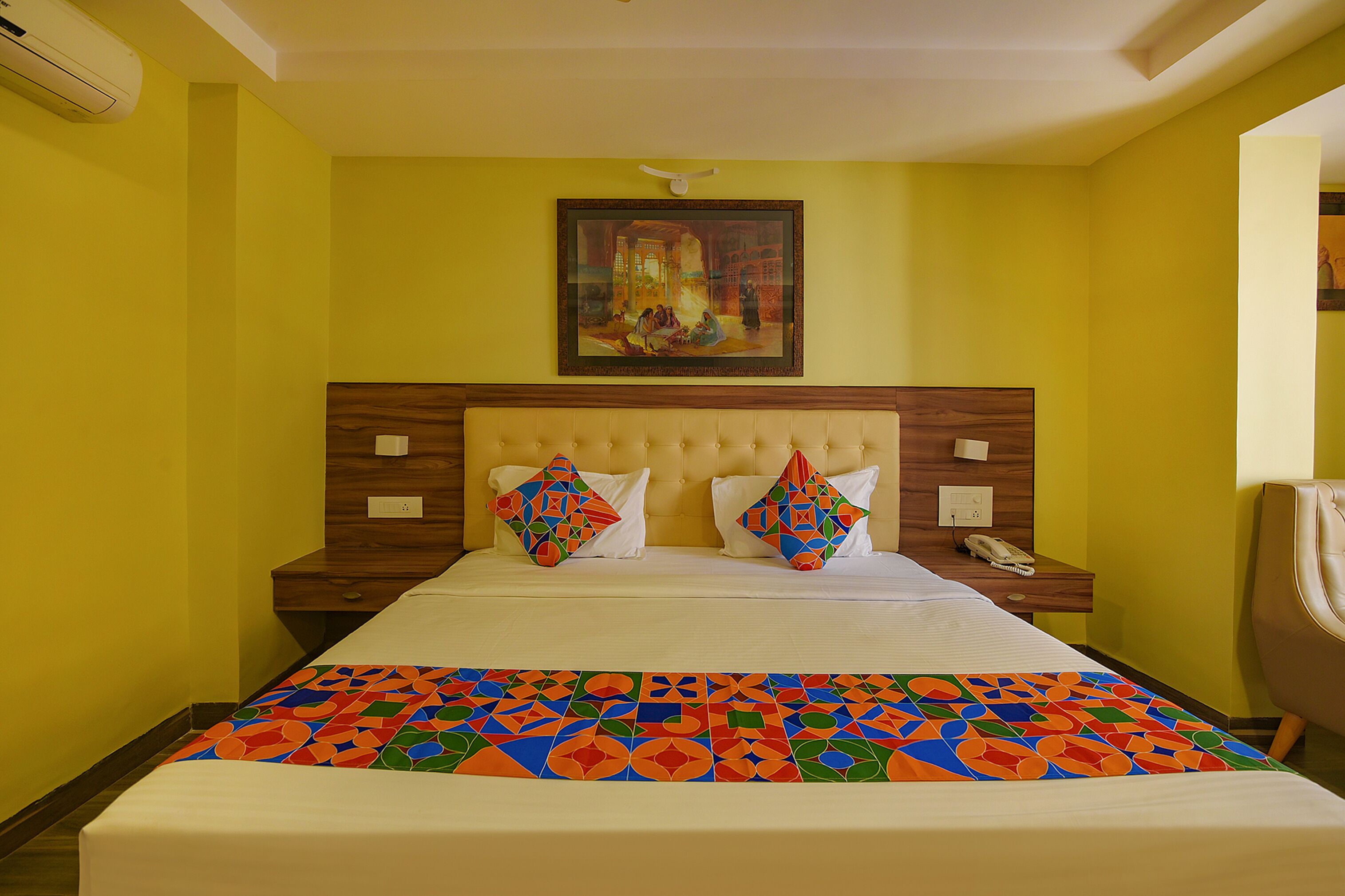 Een hotelkamer met een groot bed, een hoofdeinde, een nachtkastje en een schilderij aan de muur.