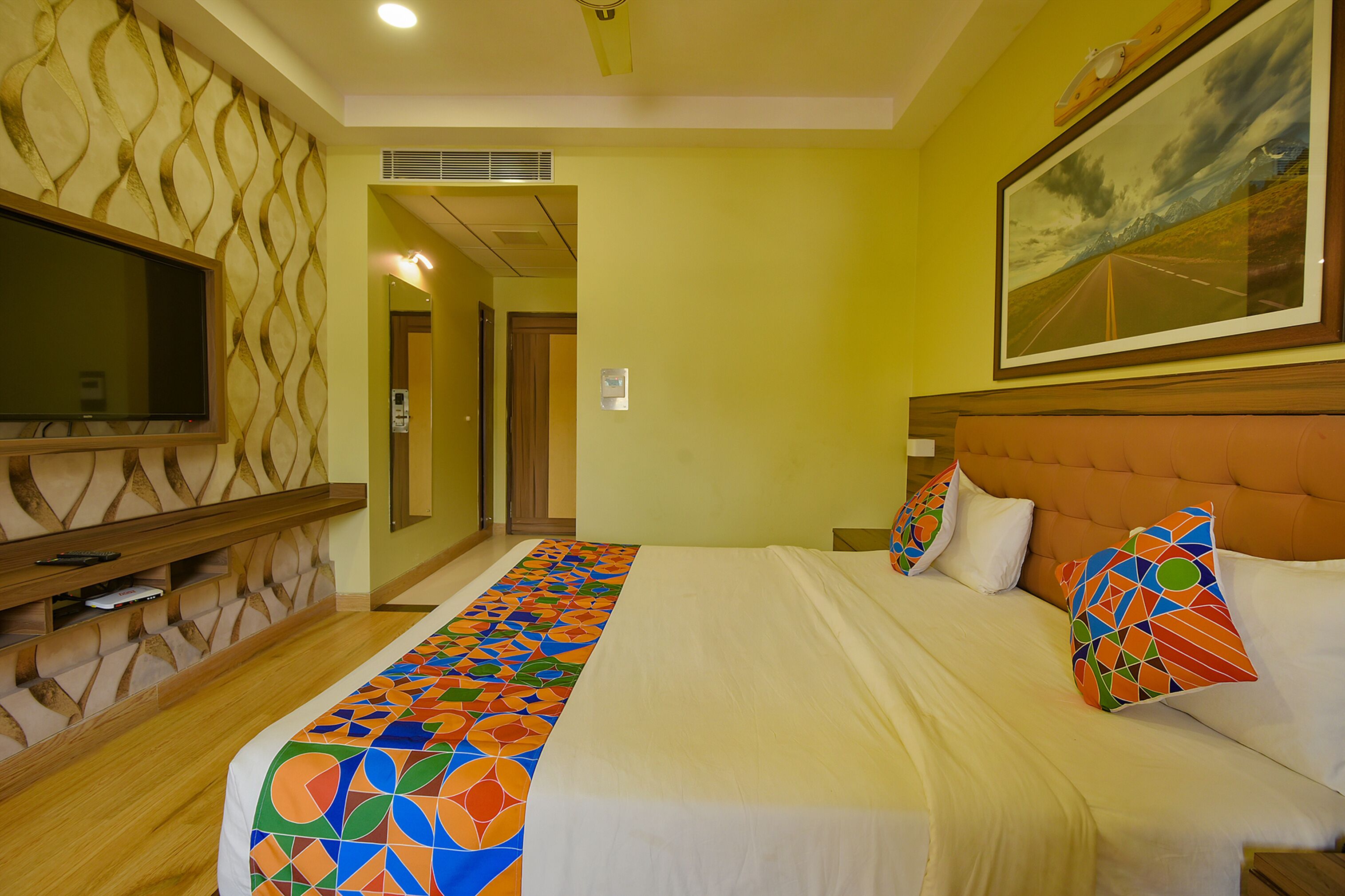A hotel room with a bed, a TV, a painting, and a patterned wall.