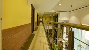 Un pasillo de hotel con piso de madera, paredes amarillas y baranda de metal.