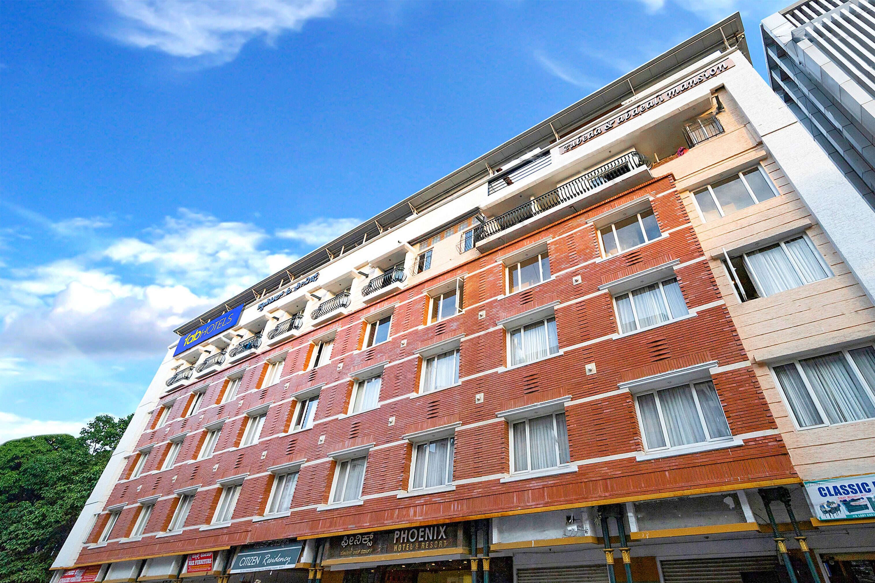 A multi-story hotel with a red brick facade, multiple balconies, and a clear blue sky.