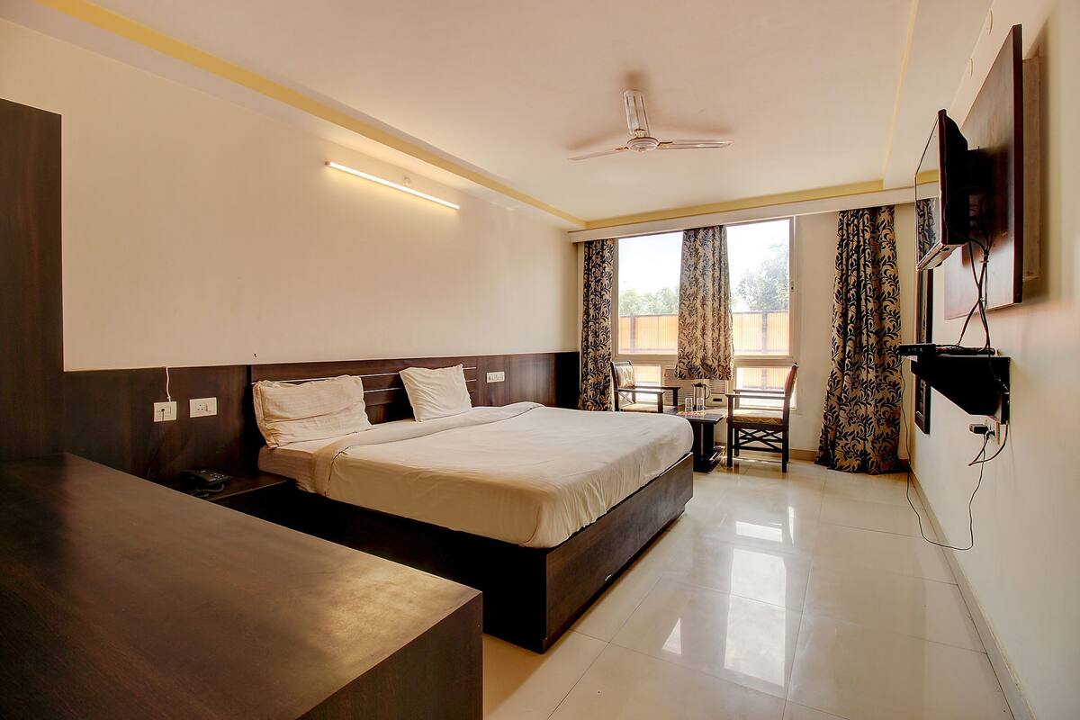 A hotel room with a bed, bedside table, desk, chair, curtains, and a TV mounted on the wall.