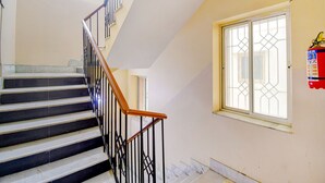 Una escalera con peldaños blancos y negros, una barandilla de madera y un extintor montado en la pared.