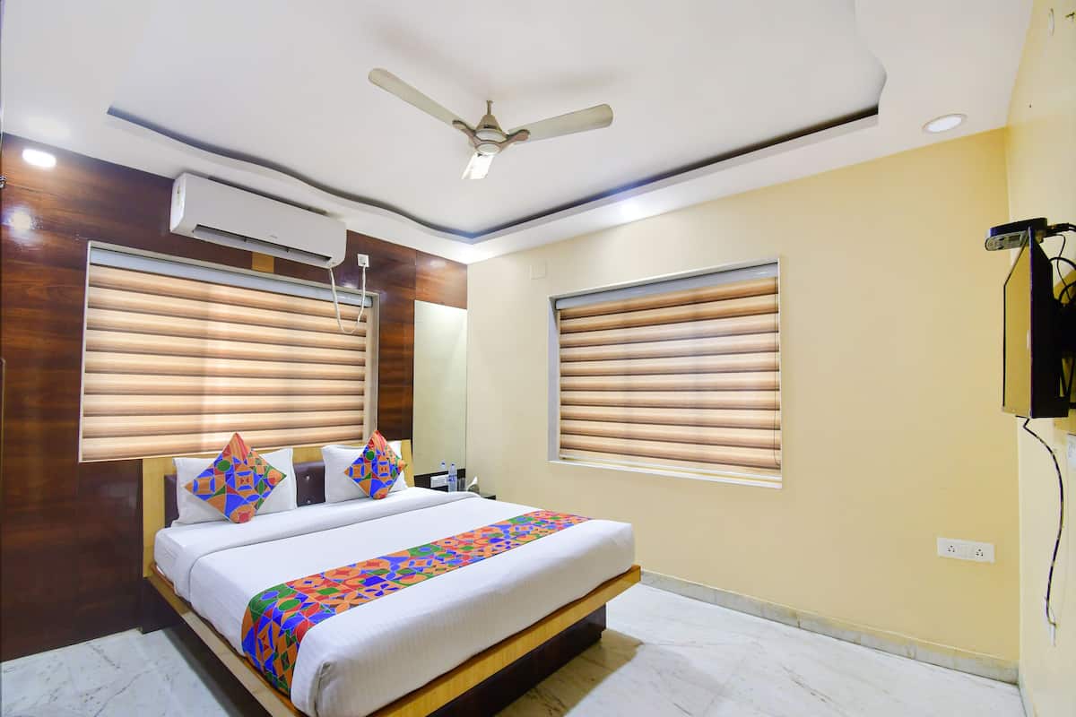Habitación de hotel con cama, ventilador de techo, aire acondicionado y dos ventanas con persianas.