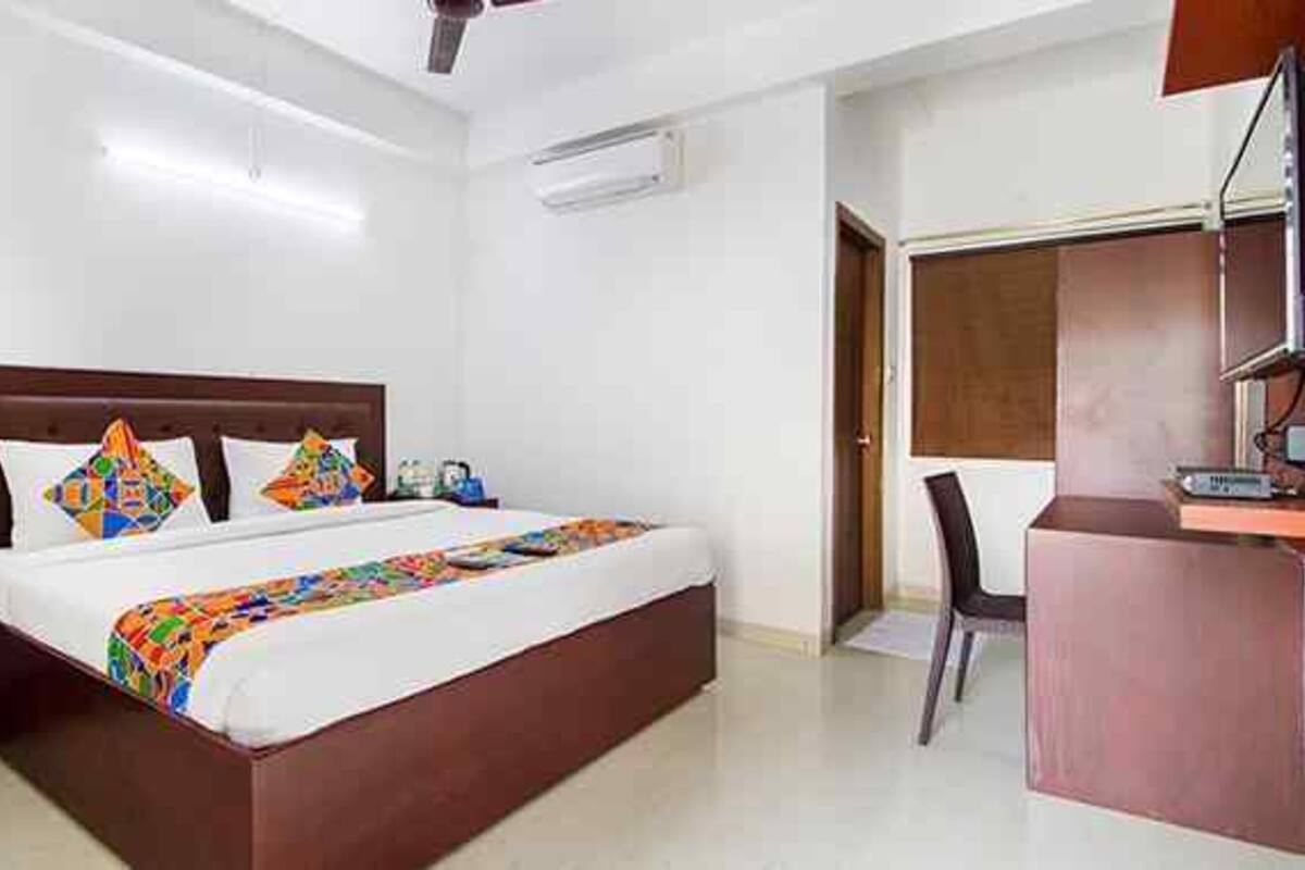 Una habitación de hotel con cama, mesita de noche, escritorio, silla y aire acondicionado.