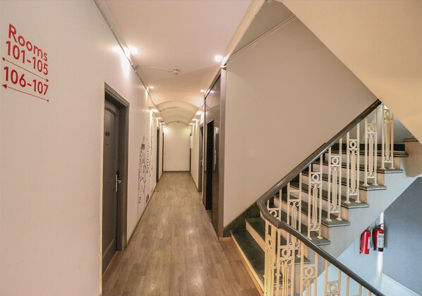 A hotel hallway with directional signs for rooms 101-105 and 106-107, a wooden floor, and a staircase with ornate railings. - Fabhotel Lord Inn (New Delhi)
