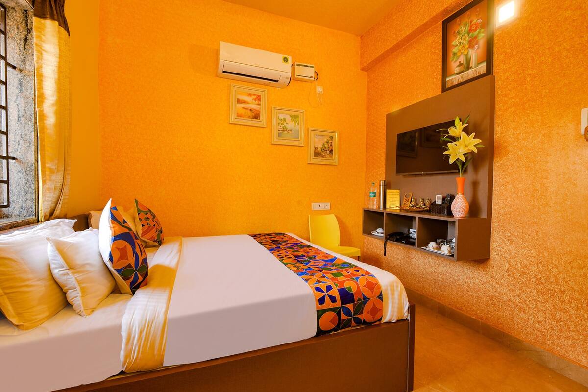 Habitació d'hotel amb un llit, aire condicionat fixat a la paret, una estant amb objectes decoratius i quadres emmarcades a la paret.