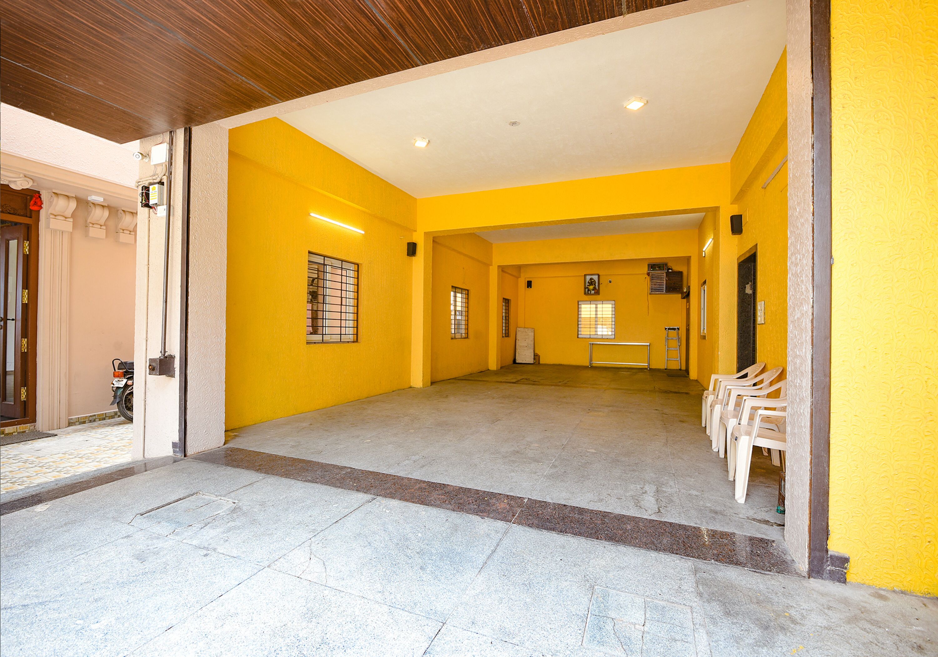 A spacious corridor with yellow walls and a tiled floor, leading to a seating area with plastic chairs.