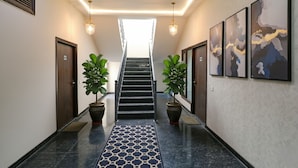 Un couloir avec un tapis à motifs, des plantes en pot, un escalier et des œuvres d’art encadrées accrochées aux murs.