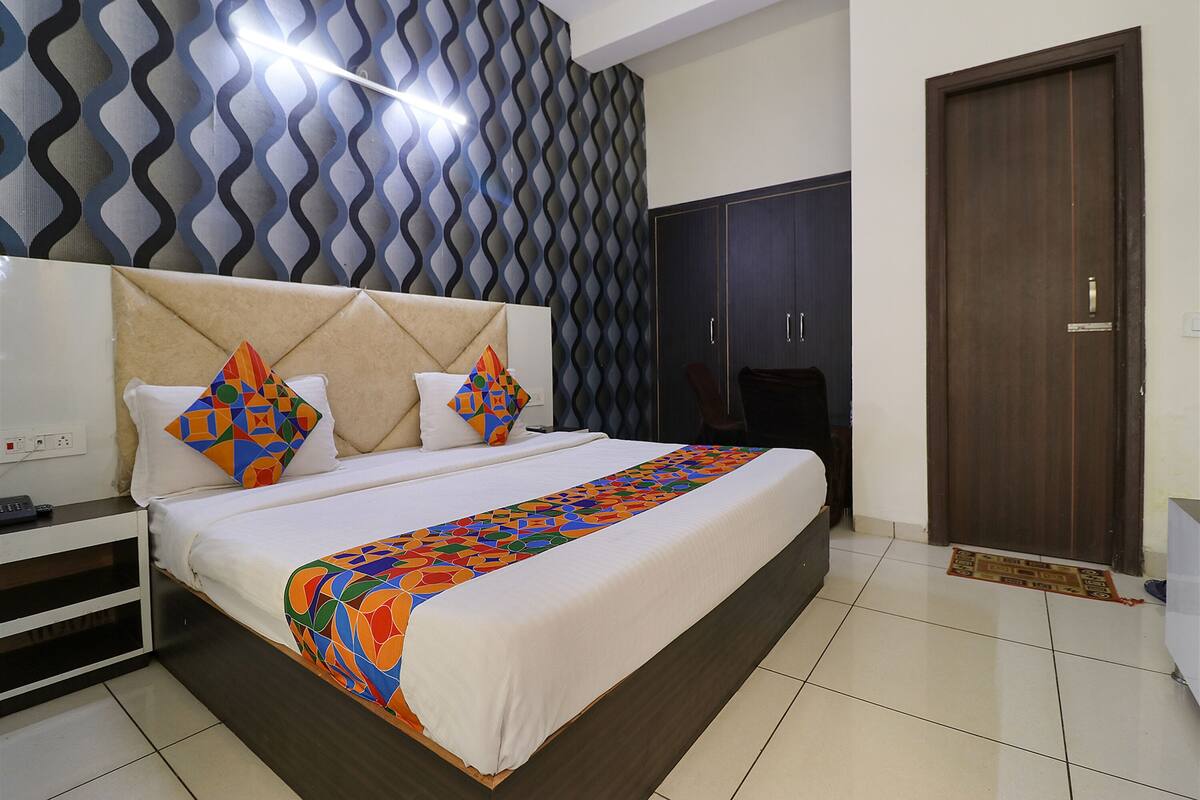 A neatly made bed with a colorful geometric-patterned bedspread, a headboard with a geometric-patterned wall behind it, and a dark wooden wardrobe.