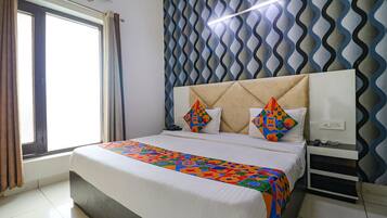 A neatly made bed with a colorful bedspread, a headboard with geometric patterns, a bedside table with a lamp, and a window with curtains.