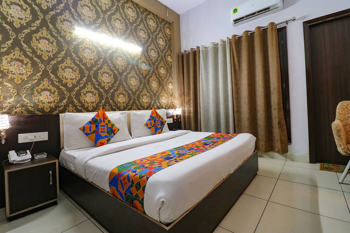 A hotel room with a large bed, a nightstand with a phone, and a patterned wallpaper.