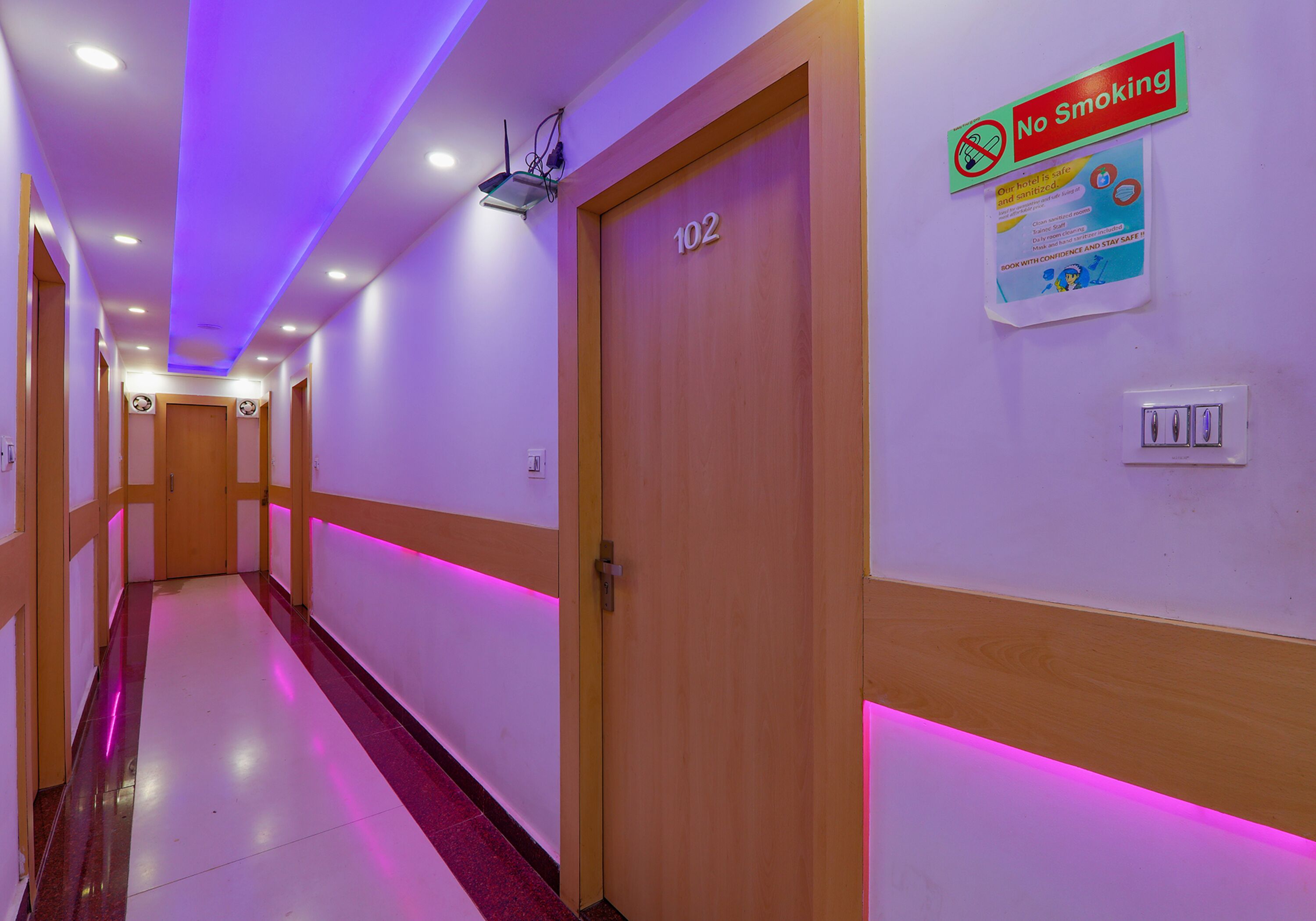 A hotel hallway with a 'No Smoking' sign, a door labeled '102', and a poster on the wall.
