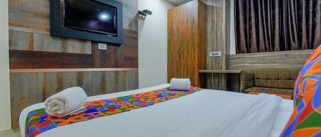 A hotel room with a bed, a TV mounted on the wall, a wooden headboard, and a curtain.