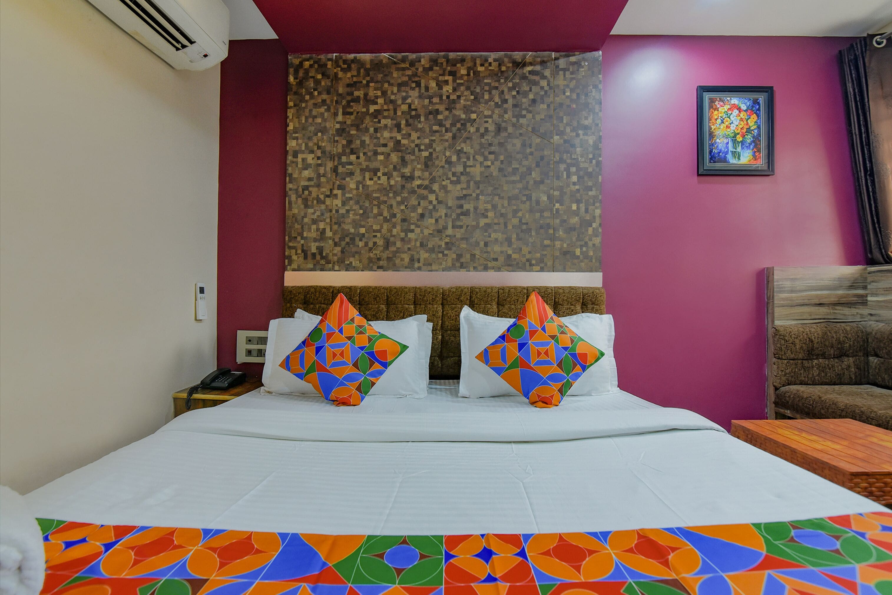 A hotel room with a bed, two pillows, a nightstand, a phone, a painting, and a couch.