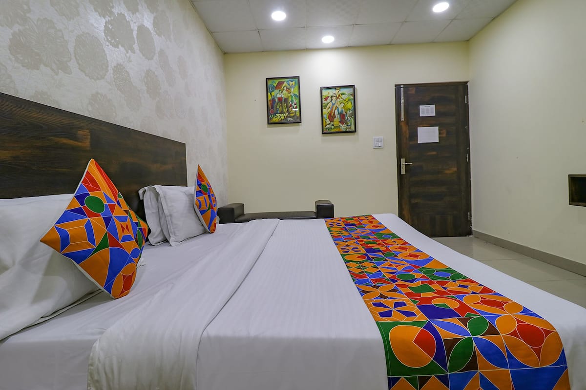 Quarto de hotel com cama, almofadas, cabeceira, porta e duas imagens emolduradas na parede.