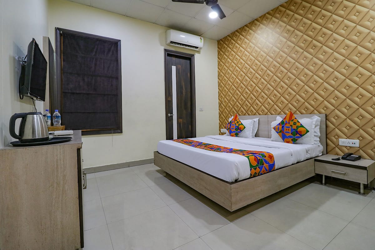 Quarto de hotel com cama, mesa de cabeceira, criado-mudo e televisão na parede.