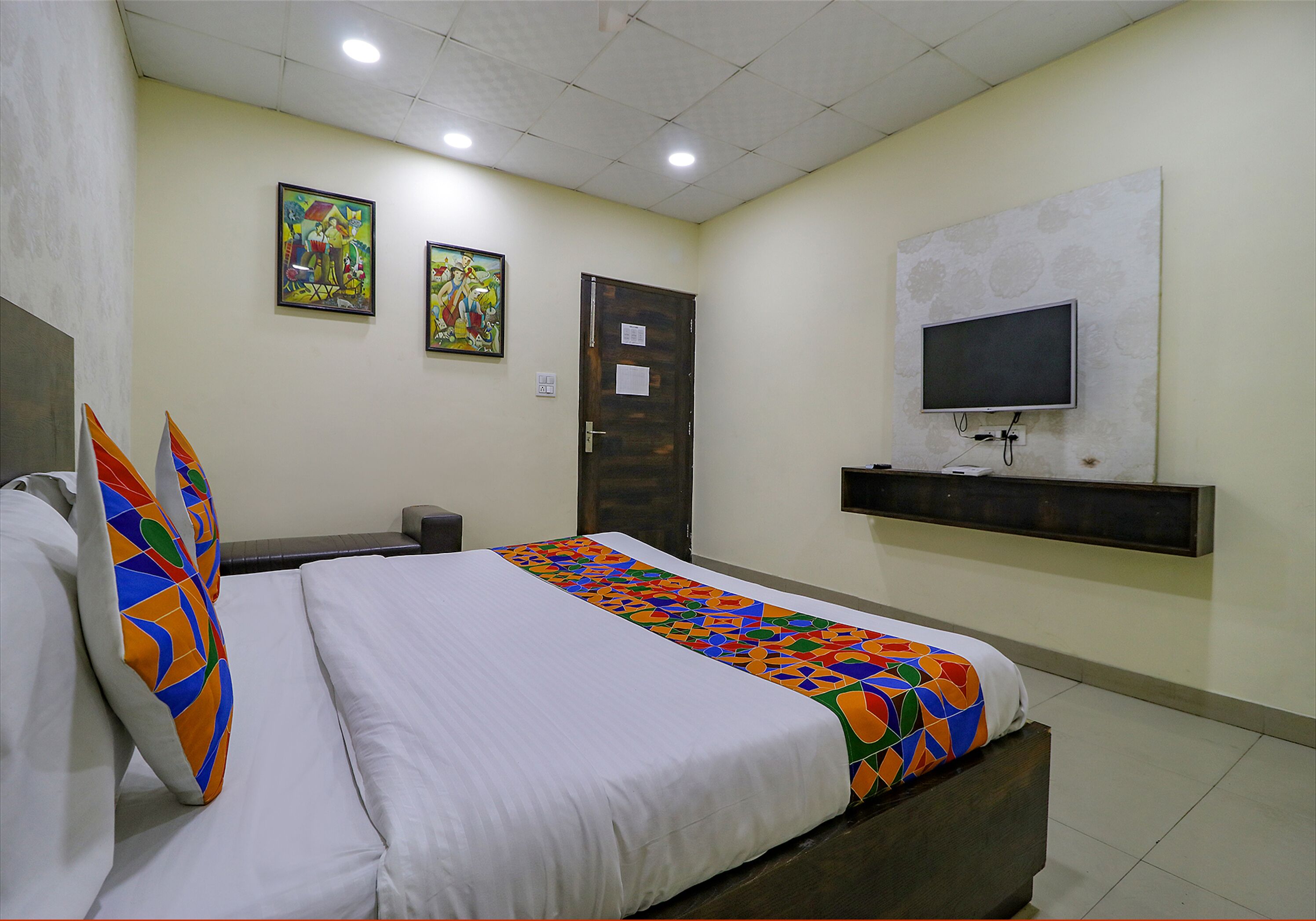 A hotel room with a bed, a TV mounted on the wall, and two framed pictures on the wall.