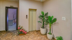 Un pasillo con un letrero de salida, un ascensor y plantas en macetas.