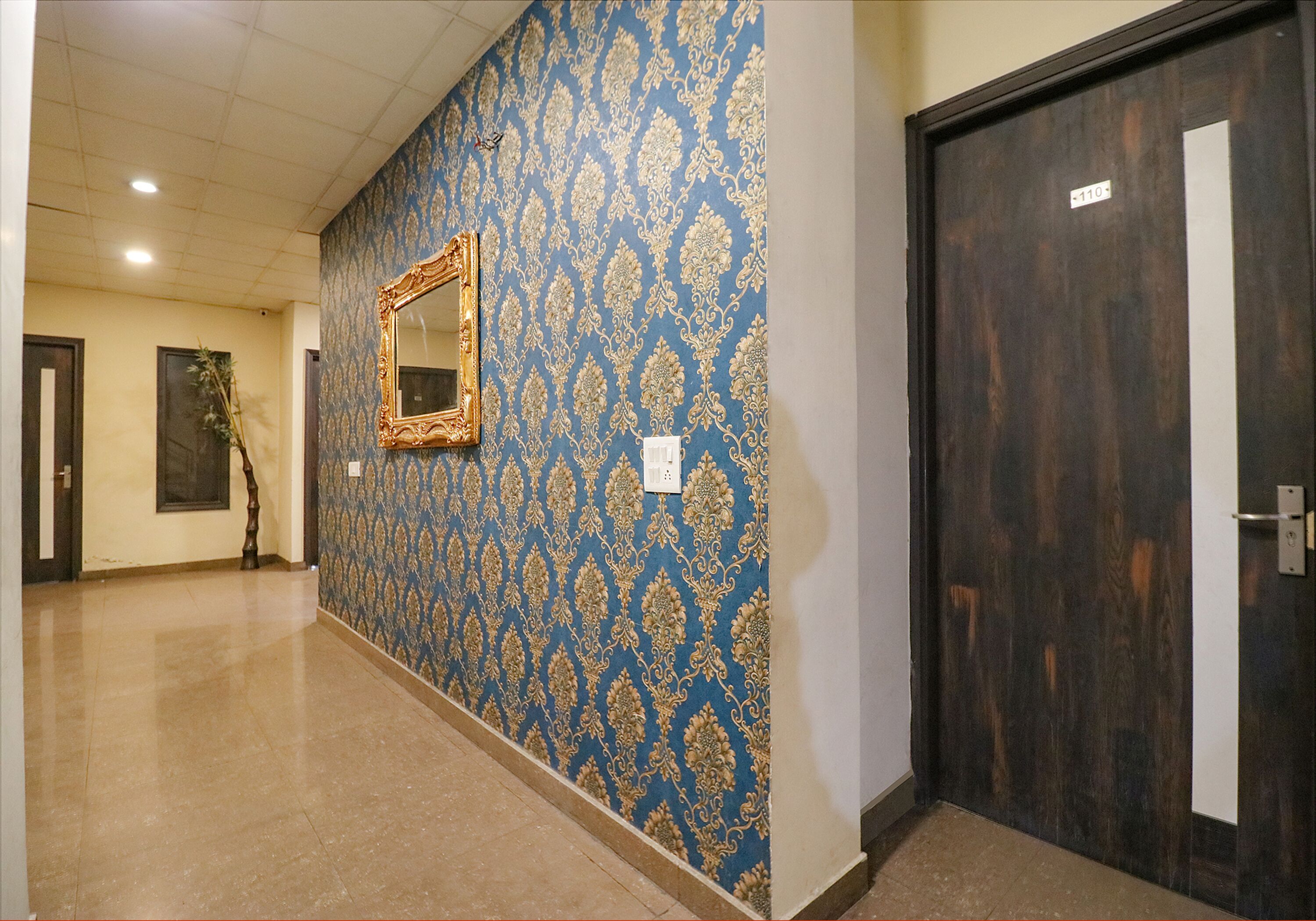 A hallway with patterned wallpaper, a mirror, and a door with a number sign.