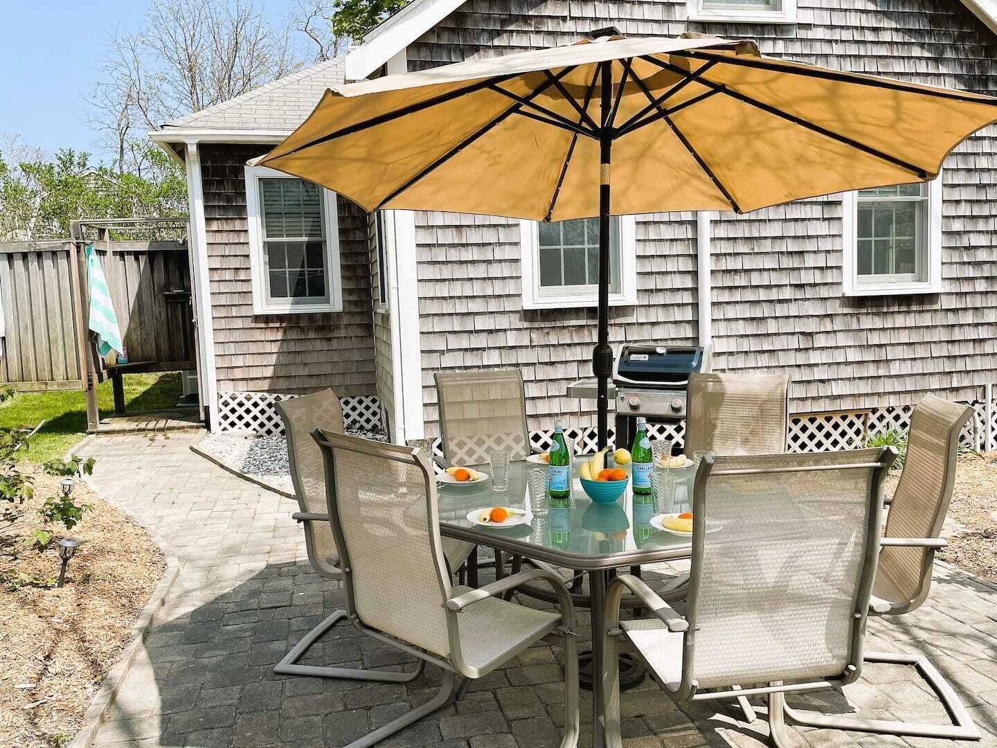 An outdoor patio with a table and chairs, a grill, and a large umbrella.