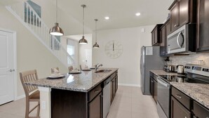 A kitchen with dark wood cabinets, a granite countertop, stainless steel appliances, and pendant lighting. - Rent This Luxury 5 Star House on Windsor Island, Orlando House 6154 (Davenport)