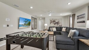 A living room with a foosball table, a gray sofa, and artwork on the walls. - Rent This Luxury 5 Star House on Windsor Island, Orlando House 6154 (Davenport)