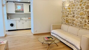 Een woonkamer met een bank, een salontafel en een keukenhoek met kasten en een wasmachine.