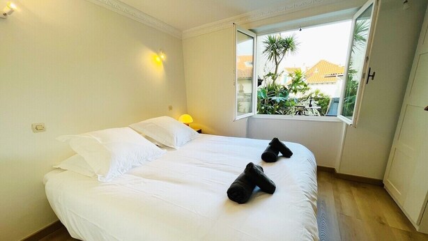 Hotelkamer met een groot bed, een raam met uitzicht op groen en gebouwen, een nachtkastje met een lamp, en een deur aan de rechterkant.