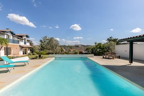 A swimming pool with lounge chairs, a pergola, and a view of a hillside.