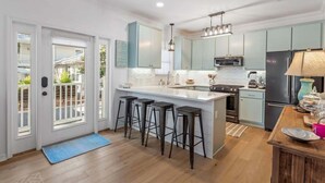 A modern kitchen with light blue cabinets, a large island with bar stools, a black refrigerator, and a pendant light above the island. - Playing Hooky! Dog Friendly- 4 Bikes- Heated Pool (Santa Rosa Beach)