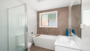 A modern bathroom with a glass shower enclosure, a white bathtub, and a sink with a mirror.