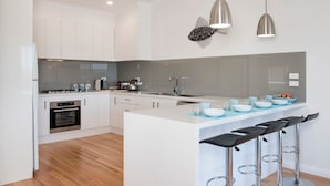 A modern kitchen with white cabinetry, stainless steel appliances, a central island with bar stools, and pendant lighting.