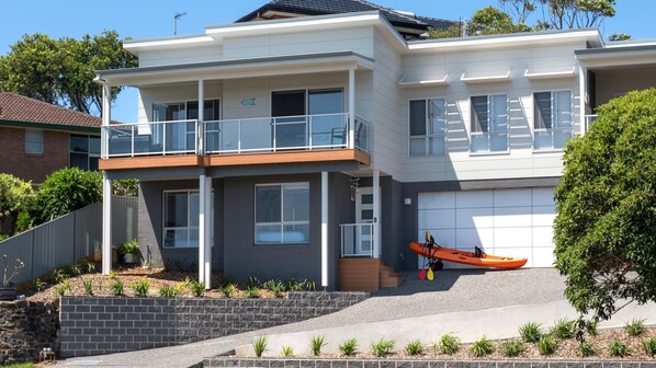 Une maison moderne à deux étages, dotée d’un balcon, d’un garage et d’un kayak.