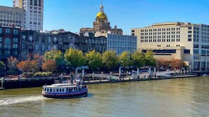 Une rivière avec un bateau, des bâtiments et, au fond, une structure remarquable surmontée d’un dôme jaune.