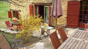Una casa de piedra con una mesa y sillas de madera afuera, un pequeño jardín y una puerta roja.