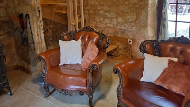 Una habitación rústica con paredes de piedra, una escalera de madera y dos sillones de cuero con cojines.