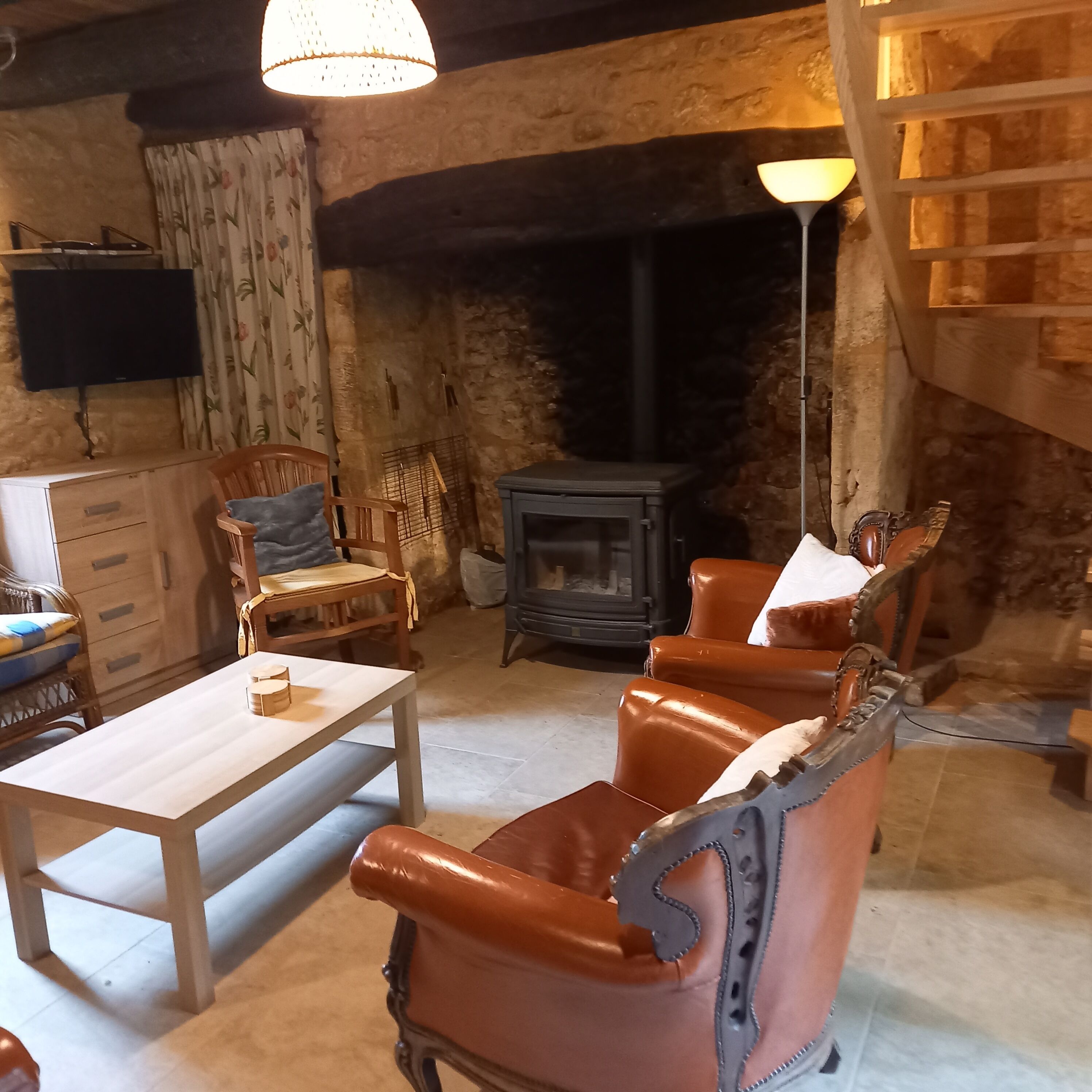 Un salón acogedor con chimenea, sillones de cuero, una mesa de madera y un televisor montado en la pared.