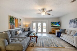A living room with a gray sectional sofa, a coffee table, a ceiling fan, and a TV on the wall.