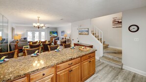 A modern kitchen with a granite countertop, wooden cabinets, and a dining area with wicker chairs.