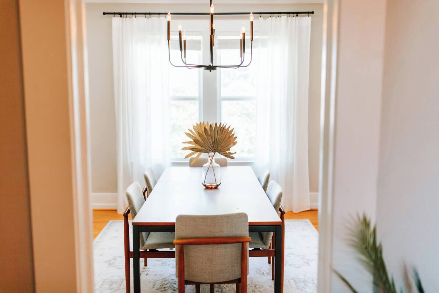 Comedor con una mesa larga, sillas, una araña y un jarrón decorativo.