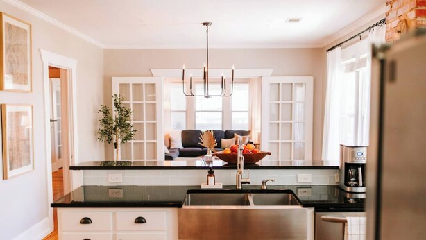 A modern kitchen with white cabinetry, a black countertop, a stainless steel sink, and a coffee maker.