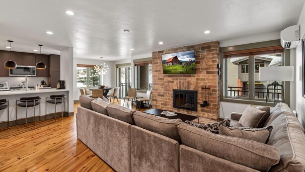 A modern living room with a sectional sofa, a fireplace, and a kitchen area with bar stools. - Bear Claw 415 on Mountain Condo with Ski-In/Ski-Out Access! (Steamboat Springs)
