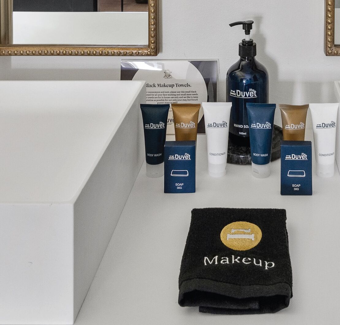 Ein Badezimmer-Waschtisch mit Spiegel, ein schwarzes Handtuch für Make-up und verschiedene Duvet-Pflegeprodukte wie Duschgel, Conditioner und Seife.
