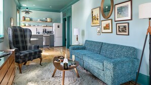 A living room with a patterned sofa, a patterned armchair, a coffee table, and a dining area with a kitchen in the background.