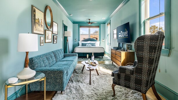 A room with a bed, a sofa, a chair, a TV, and a window with a view.