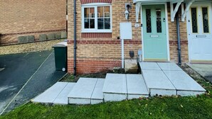 Una casa de ladrillo de dos pisos con una puerta verde, un pequeño porche y una antena parabólica visible.